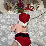Aurora is registered to the contest to win money with this photo: baby, blanket, christmas_tree, christmas_lights, ornament, holiday_decor, festive, crocheted_clothing, santa_hat, santa_outfit, reindeer_figurine, joy_sign, floor, indoor, toddler, red_clothing, white_tree, colorful_lights, festivity, holiday_theme