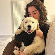 Milo participe au concours pour gagner de l'argent avec cette photo : affection, casual_clothing, companion, couch, curly_hair, dog, floor_tiles, golden_retriever, happy, hugging, indoor, love, person, pet, puppy, radiator, sitting, smiling, tattoo, white_wall