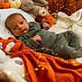 baby, infant, blanket, stuffed_animal, pumpkin, fairy_lights, orange_blanket, green_outfit, couch, cozy, soft_toys, autumn, cute, indoors, portrait, newborn, relaxing, decor, warm_lighting, child