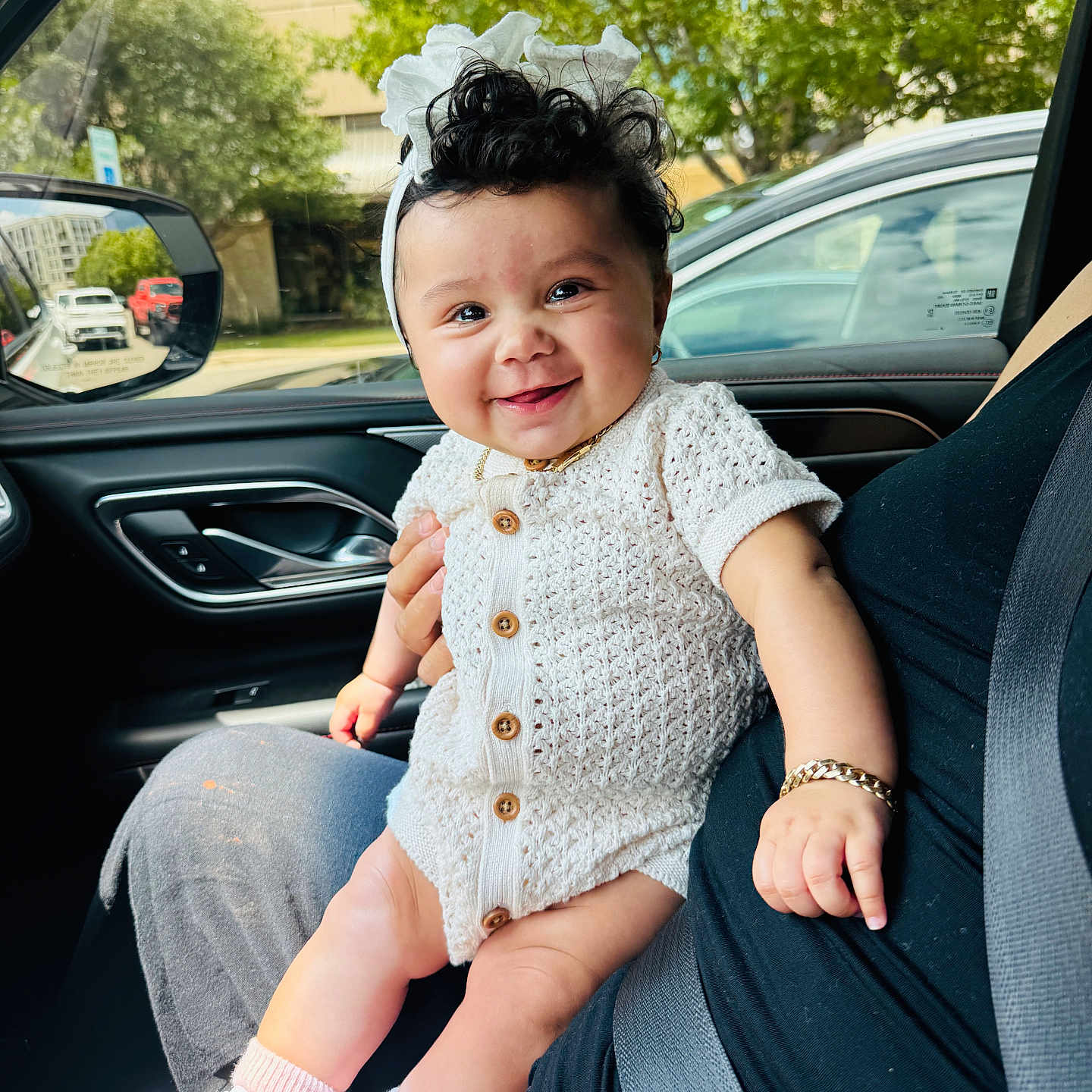 Daniela joined the competition — help win amazing prizes! baby, child, smile, curly_hair, white_romper, bow, bracelet, car_interior, seatbelt, adult, window, trees, daylight, happy, cute, footwear, socks, hand, portrait, person