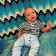 Caleb is registered to the contest to win money with this photo: baby, infant, striped_shirt, light_blue_pants, socks, blanket, knitted_blanket, blue, black, white, pattern, face, cute, indoors, child, person, seated, expression, cozy, soft