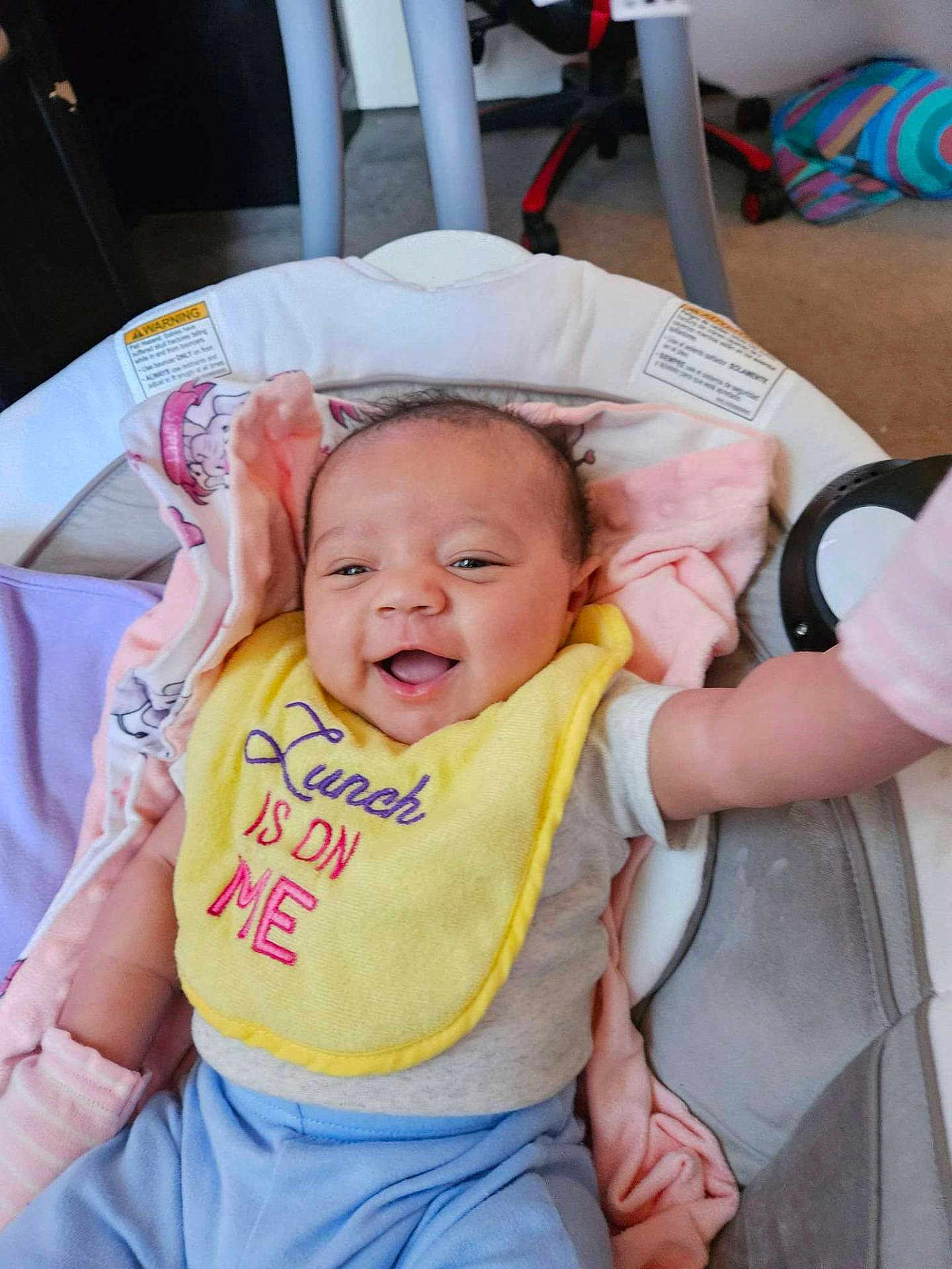 Cherish is registered to the contest to win money with this photo: baby, smiling, bib, yellow_bib, baby_seat, blanket, indoor, happy, infant, clothing, blue_pants, pink_blanket, face, person, child, cute, young, seat, comfort, home