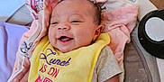 Cherish is registered to the contest to win money with this photo: baby, smiling, bib, yellow_bib, infant, cushion, blanket, baby_seat, indoor, happy, person, child, cute, clothing, toy, pink_gloves, face, head, comfort, infancy