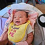 baby, smiling, bib, yellow_bib, infant, cushion, blanket, baby_seat, indoor, happy, person, child, cute, clothing, toy, pink_gloves, face, head, comfort, infancy