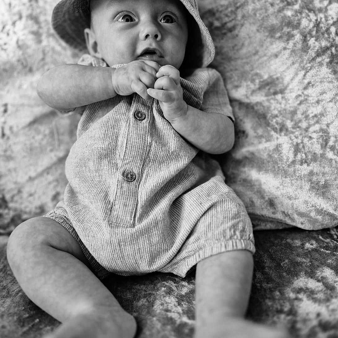 Caven-John is registered to the contest to win money with this photo: baby, bodypart, bonnet, cap, clothing, face, finger, hand, happy, hat, head, hood, pants, person, photography, portrait, shorts, sitting, smile, sunhat