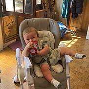 Mathys participe au concours pour gagner de l'argent avec cette photo : baby, high_chair, cup, indoor, sunlight, window, floor, coat_stand, clothing, socks, tiled_floor, child, smiling, seat, furniture, room, playful, relaxed, drink, infant