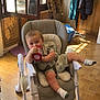 baby, high_chair, cup, indoor, sunlight, window, floor, coat_stand, clothing, socks, tiled_floor, child, smiling, seat, furniture, room, playful, relaxed, drink, infant