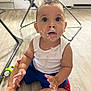 toddler, child, baby, messy_face, cream, yogurt, white_tank_top, blue_shorts, sitting, floor, wooden_floor, indoor, curious_expression, wide_eyes, barefoot, toy, furniture, folding_chair, door, home
