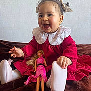 Leen a rejoint le concours — aidez-le/la à gagner de superbes lots ! child, baby, toddler, smiling, red_dress, lace_collar, bow_hair, doll, toy, sitting, portrait, indoor, white_wall, plush_blanket, shoes, socks, happy, face, hands, long_hair