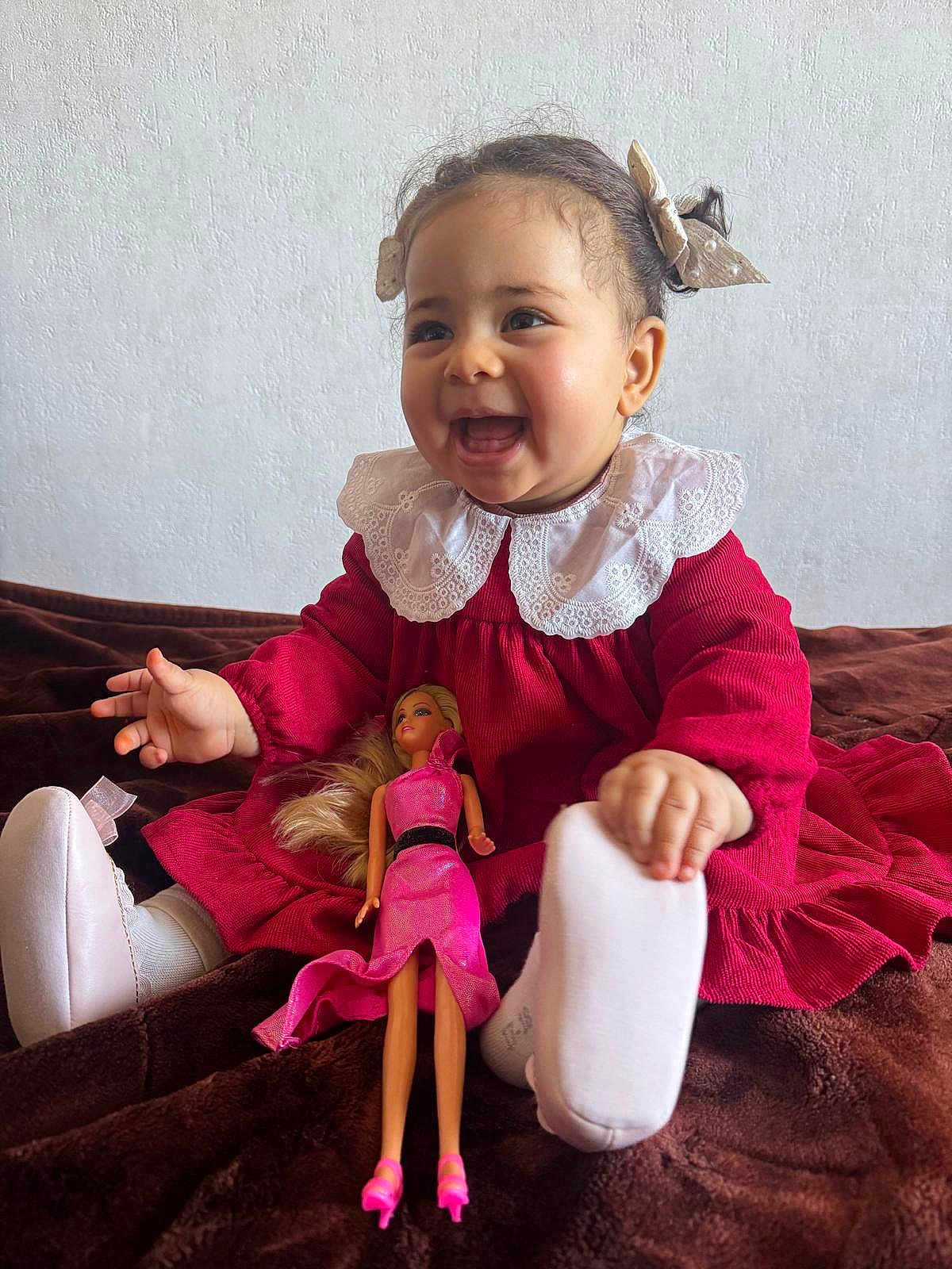 Leen a rejoint le concours — aidez-le/la à gagner de superbes lots ! child, baby, toddler, smiling, red_dress, lace_collar, bow_hair, doll, toy, sitting, portrait, indoor, white_wall, plush_blanket, shoes, socks, happy, face, hands, long_hair