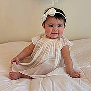 Vianka is registered to the contest to win money with this photo: baby, bed, blanket, bow, child, cozy, cute, dress, face, happy, headband, indoors, infant, portrait, sitting, skin, smiling, soft_lighting, white, young
