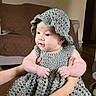Annaliese is registered to the contest to win money with this photo: baby, child, clothing, couch, crocheted_dress, crocheted_hat, curious, cute, face, fashion, hands, human, indoor, infant, living_room, person, portrait, seated, skin, soft_lighting