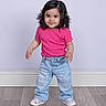 child, toddler, girl, portrait, smiling, standing, pink_shirt, jeans, sneakers, curly_hair, bracelet, studio, indoors, floor, wall, fashion, colorful_shoes, happy, full_body, photography