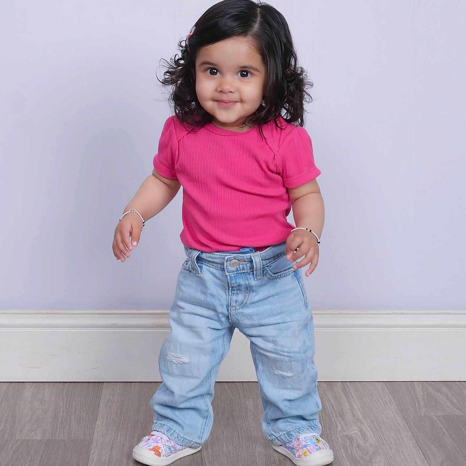 Mehar is registered to the contest to win money with this photo: child, toddler, girl, portrait, smiling, standing, pink_shirt, jeans, sneakers, curly_hair, bracelet, studio, indoors, floor, wall, fashion, colorful_shoes, happy, full_body, photography