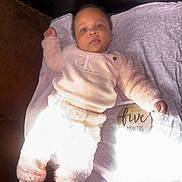Sevyn is registered to the contest to win money with this photo: baby, infant, blanket, clothing, soft_texture, pink, white, wooden_sign, sign, face, person, laying_down, indoors, cute, young_child, sleepwear, feet, hand, portrait, calm