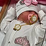 baby, sleeping, pacifier, hat, pink_bow, white_outfit, rhinestones, crown_patch, gold_chain, blanket, infant, cute, peaceful, soft, clothing, child, resting, indoors, newborn, face