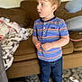 child, toddler, barefoot, striped_shirt, jeans, indoor, carpet, couch, blanket, furniture, curly_hair, person, standing, casual_clothing, home, portrait, side_view, young_child, curious, room