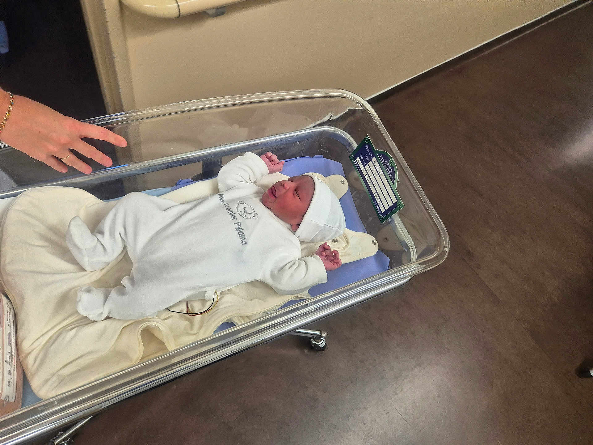 Raphaël a rejoint le concours — aidez-le/la à gagner de superbes lots ! newborn, baby, hospital, bassinet, white_clothing, hat, blanket, hand, floor, medical_equipment, infant, sleeping, person, bed, hospital_room, cute, small, resting, child, healthcare