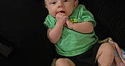 Jameson is registered to the contest to win money with this photo: baby, infant, child, green_shirt, black_shorts, couch, blanket, hand_in_mouth, indoors, furniture, person, sitting, cute, young, skin, face, foot, relaxing, home, casual