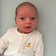 Theo is registered to the contest to win money with this photo: baby, infant, face, eyes, white_onesie, duck_embroidery, clothing, newborn, portrait, cute, child, soft_texture, lying_down, expression, skin, head, person, background, closeup, light_blue