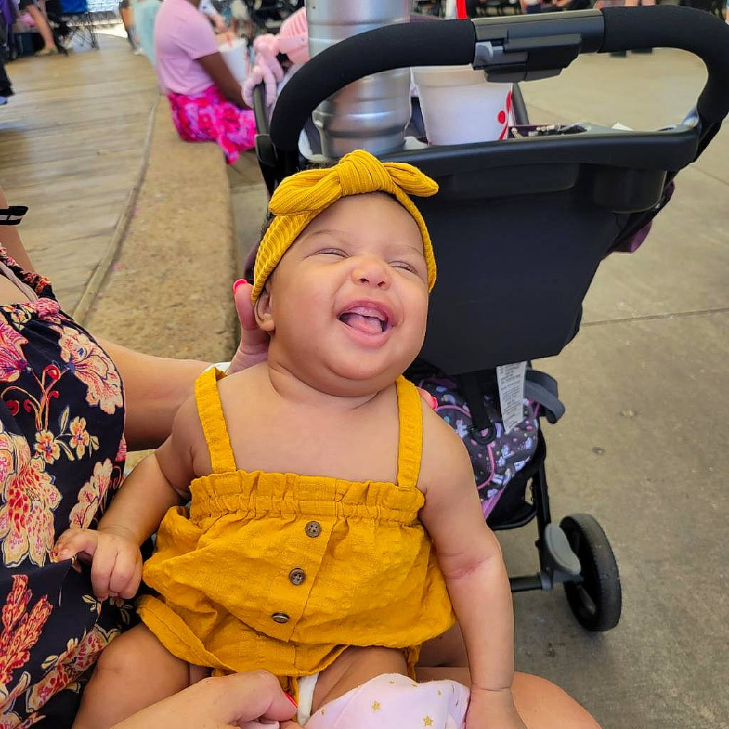 Amyah is registered to the contest to win money with this photo: baby, baby_carriage, baby_toddler_clothing, chair, child, event, facial_expression, fun, happy, headwear, leisure, person, pink, product, recreation, skin, snapshot, tire, toddler, travel