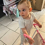 Kalysta a rejoint le concours — aidez-le/la à gagner de superbes lots ! child, clothing, curious, drying_rack, floor, hair_tie, home, indoor, patterned_pants, pink, playtime, plush_toy, sneakers, standing, stroller, tiles, toddler, toy, white_shirt, young_child