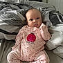 baby, infant, pink_onesie, hearts, bed, blanket, patterned_blanket, tongue_out, cute, child, indoors, person, sleepwear, soft_lighting, home, playful, lying_down, newborn, small_person, comfort