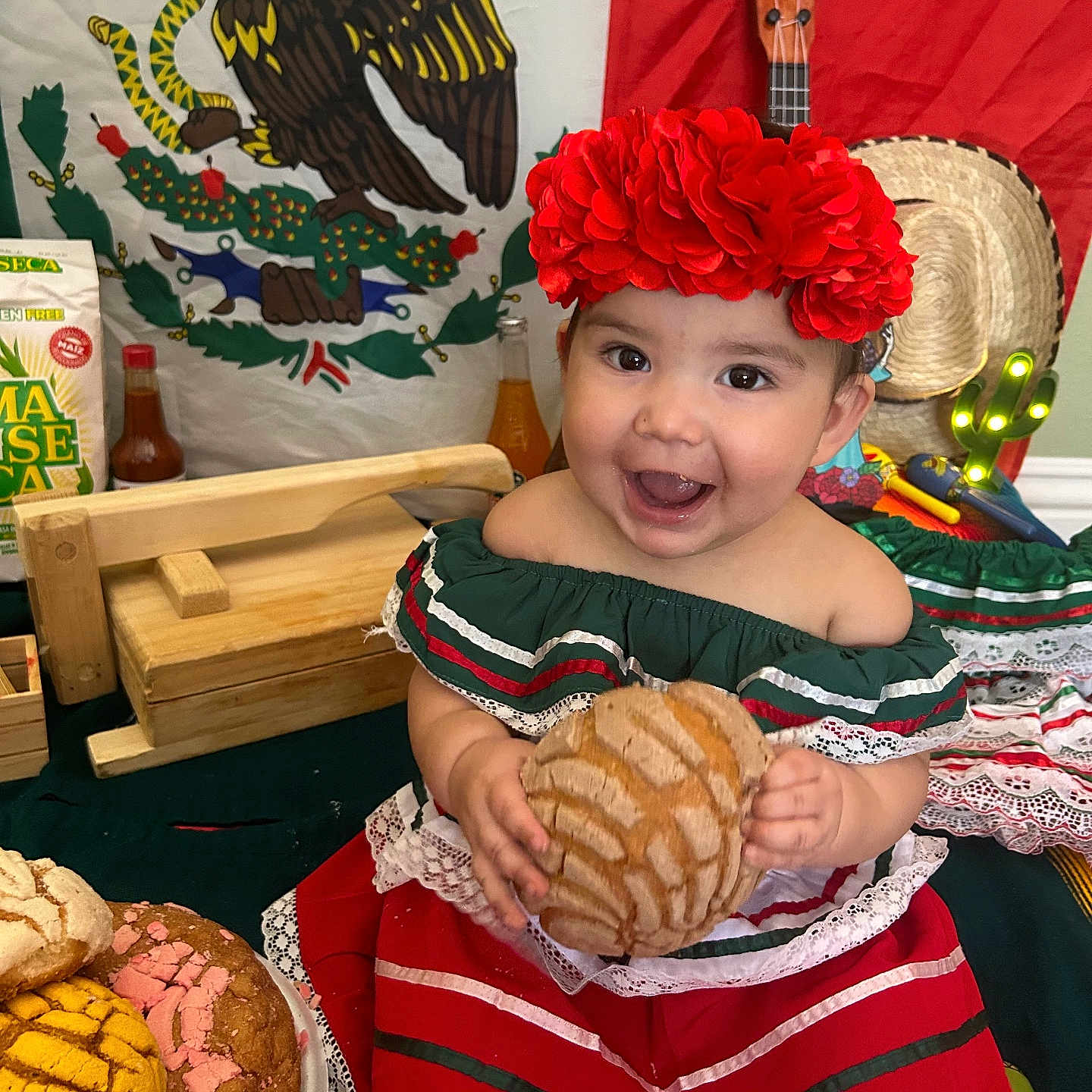 Hailey joined the competition — help win amazing prizes! bread, celebration, child, concha_bread, decorations, food, green, guitar, happy, indoors, mexican_flag, pastry, red, red_flower_headband, smiling, sombrero, table, toddler, traditional_clothing, white