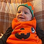 Luca joined the competition — help win amazing prizes! baby, child, pumpkin_costume, orange_clothing, hat, smiling, plaid_blanket, indoor, cute, portrait, happy, infant, cozy, black_sleeves, festive, holiday, seasonal, young_child, seated, costume