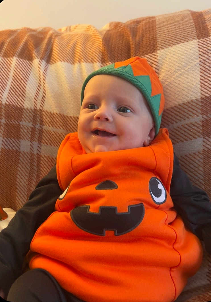 Luca joined the competition — help win amazing prizes! baby, child, pumpkin_costume, orange_clothing, hat, smiling, plaid_blanket, indoor, cute, portrait, happy, infant, cozy, black_sleeves, festive, holiday, seasonal, young_child, seated, costume