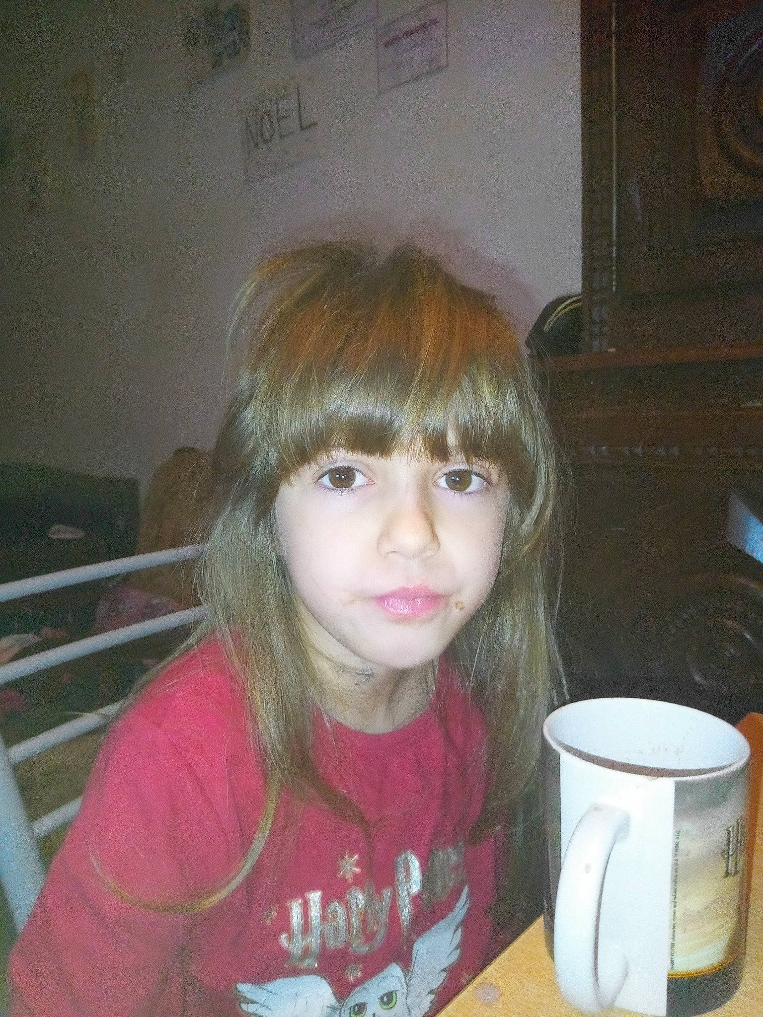 Carmen participe au concours pour gagner de l'argent avec cette photo : bangs, blond, brown_hair, chair, cheek, child, chin, coffee_cup, cup, drinkware, fun, iris, layered_hair, person, serveware, sitting, surfer_hair, t_shirt, table, tableware