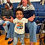 toddler, child, woman, people, indoor, gymnasium, bleachers, casual_clothing, jeans, sneakers, smile, happy, supporting, spectators, headband, glasses, floor, seating, wheelchair, adult