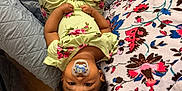 Zariah joined the competition — help win amazing prizes! baby, pacifier, upside_down, floral_outfit, blanket, bed, socks, carpet, shoe, person, indoor, cute, child, pattern, cozy, infant, clothing, hair, footwear, relaxing