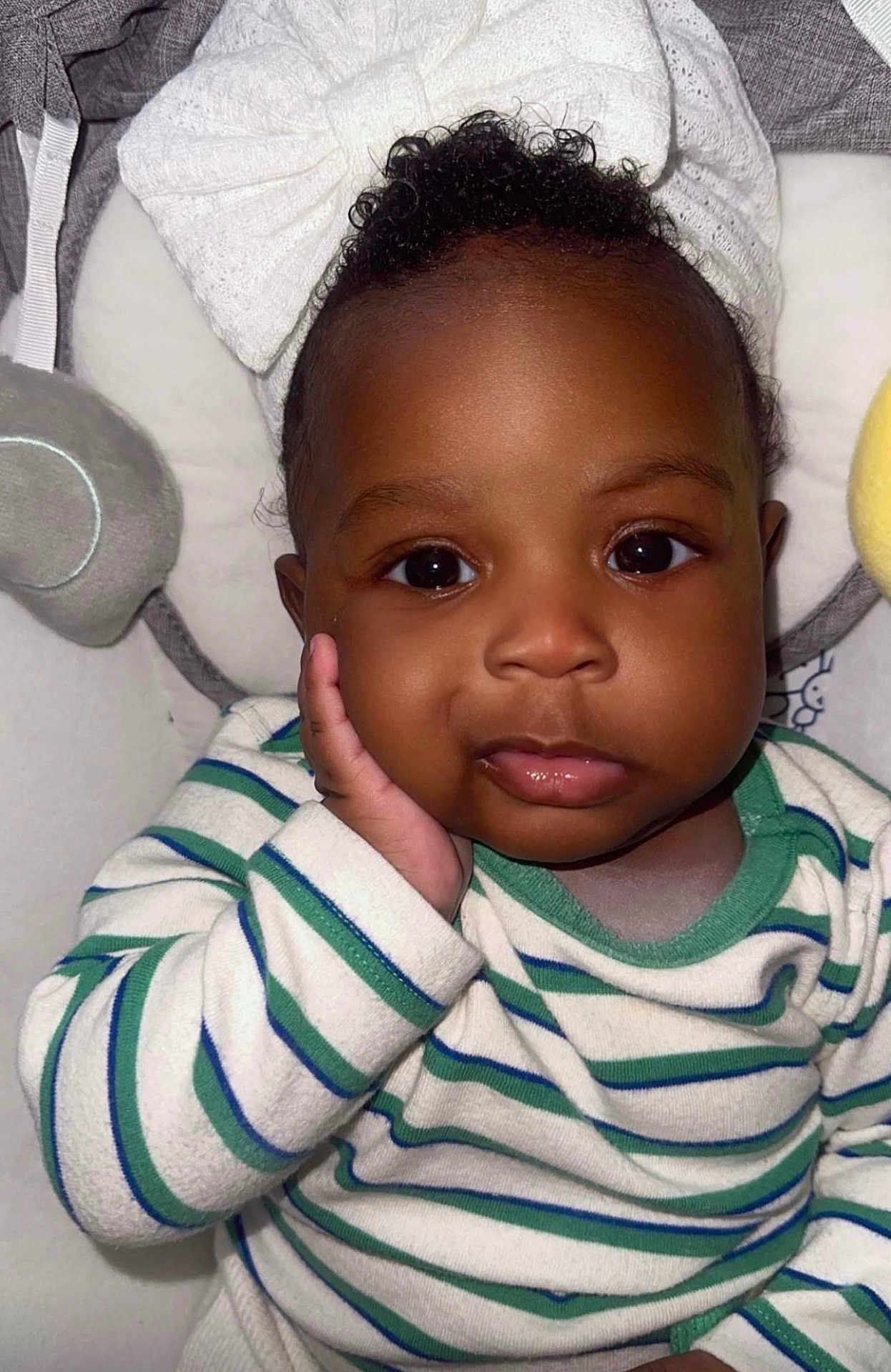 Ariah joined the competition — help win amazing prizes! baby, child, infant, face, hand, striped_clothing, bow, cute, portrait, close_up, curly_hair, sleeping_area, soft_toys, cozy, expression, skin, eyes, mouth, headwear, comfortable