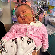 Olivia is registered to the contest to win money with this photo: baby, sleeping, pink_sweater, onesie, medical_tube, hospital, newborn, person, infant, cute, care, hand, pajamas, indoor, healthcare, child, face, resting, knitted, treatment