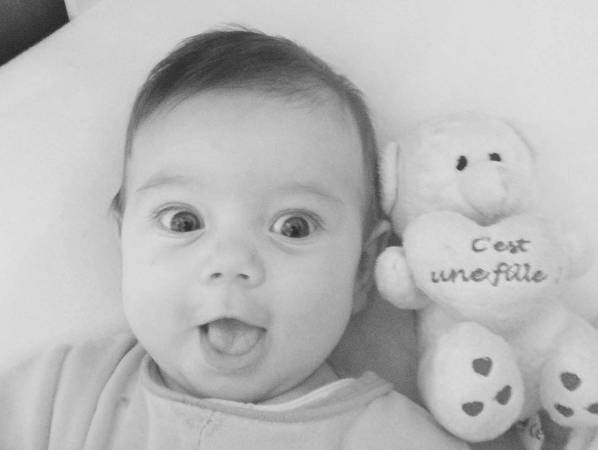 Flora participe au concours pour gagner de l'argent avec cette photo : baby, bed, black_and_white, child, close_up, clothing, cute, expression, face, heart, indoors, infant, mouth_open, plush_toy, portrait, sleeping_area, soft_texture, teddy_bear, text, wide_eyes