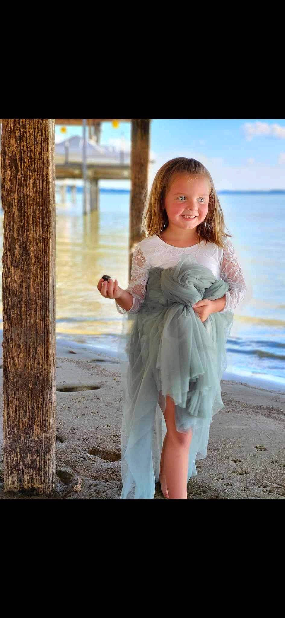 Presley is registered to the contest to win money with this photo: beach, clothing, day_dress, dress, flash_photography, gesture, happy, joy, lake, long_hair, people_in_nature, person, shoulder, sky, sleeve, smile, standing, sunlight, toddler, waist