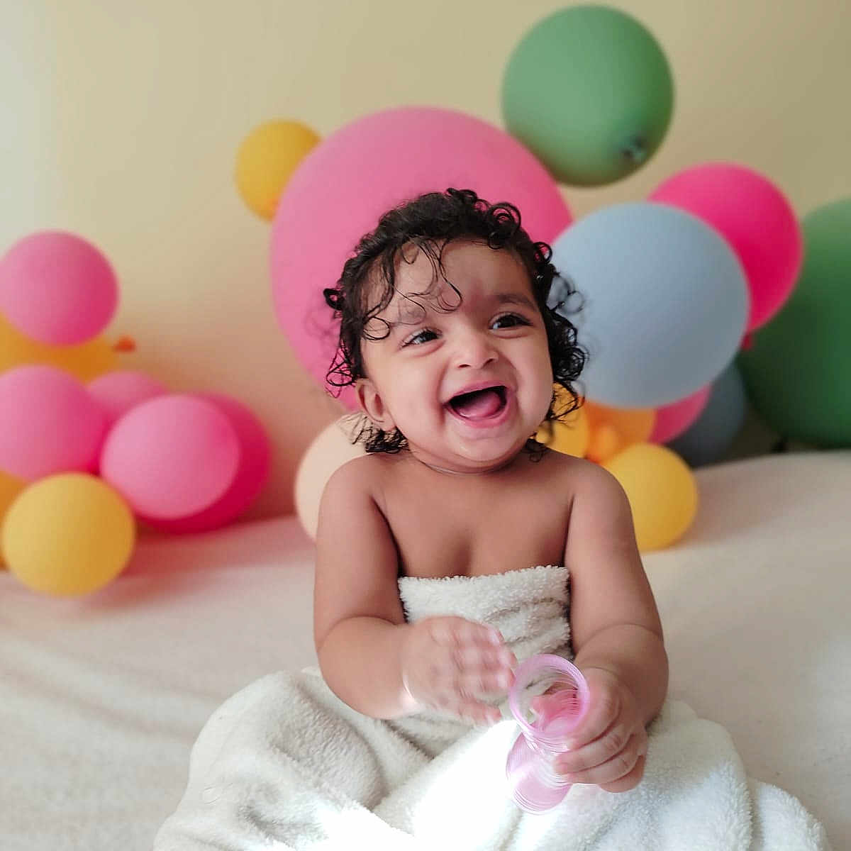 Jeshna joined the competition — help win amazing prizes! baby, balloons, celebration, child, colorful, curly_hair, cute, fun, happy, indoor, infant, joyful, laughing, pink_toy, playful, portrait, smiling, soft_texture, towel, toy