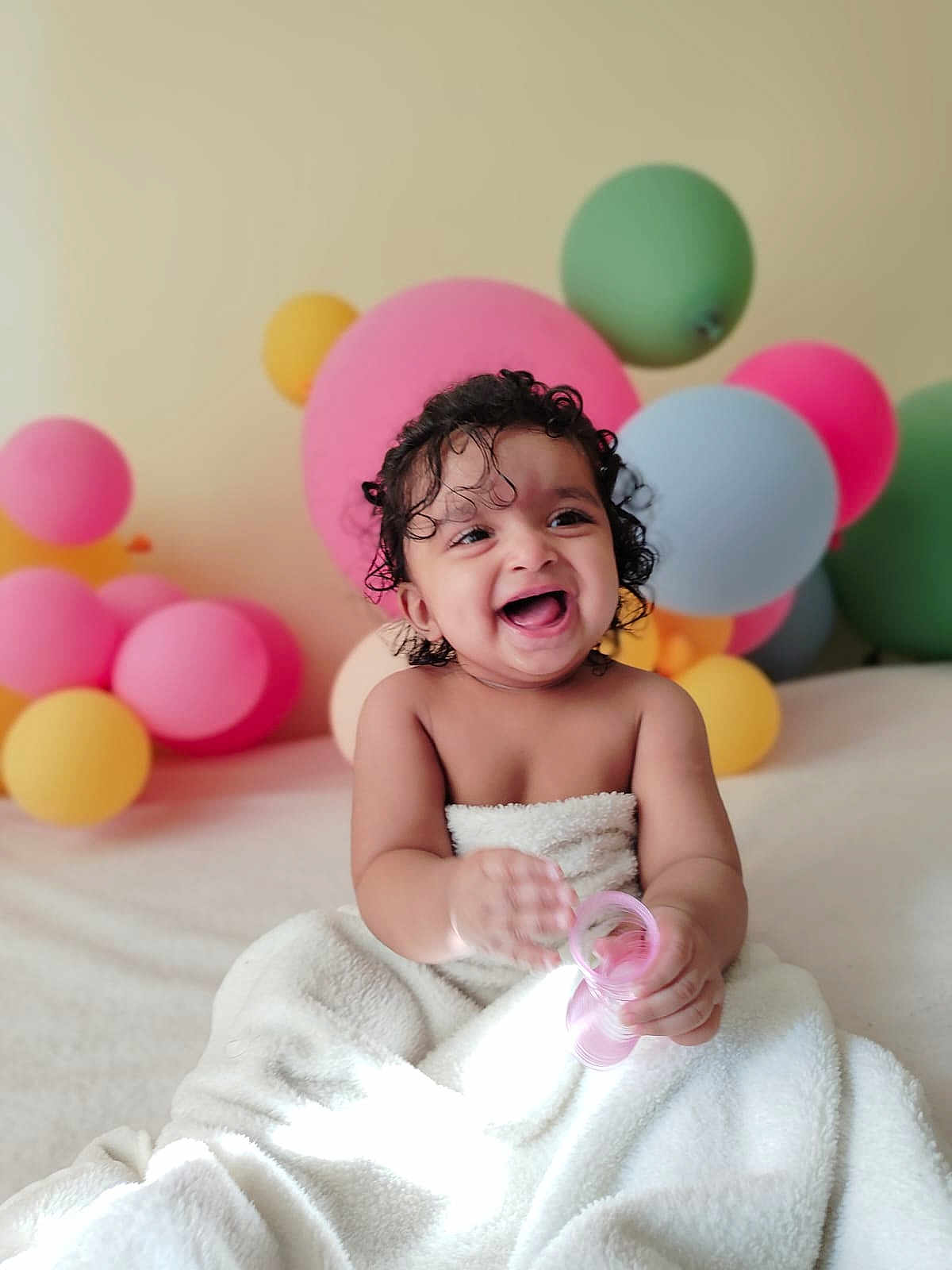 Jeshna joined the competition — help win amazing prizes! baby, child, smiling, laughing, towel, curly_hair, toy, pink_toy, balloons, colorful, indoor, portrait, happy, cute, infant, celebration, soft_texture, playful, fun, joyful