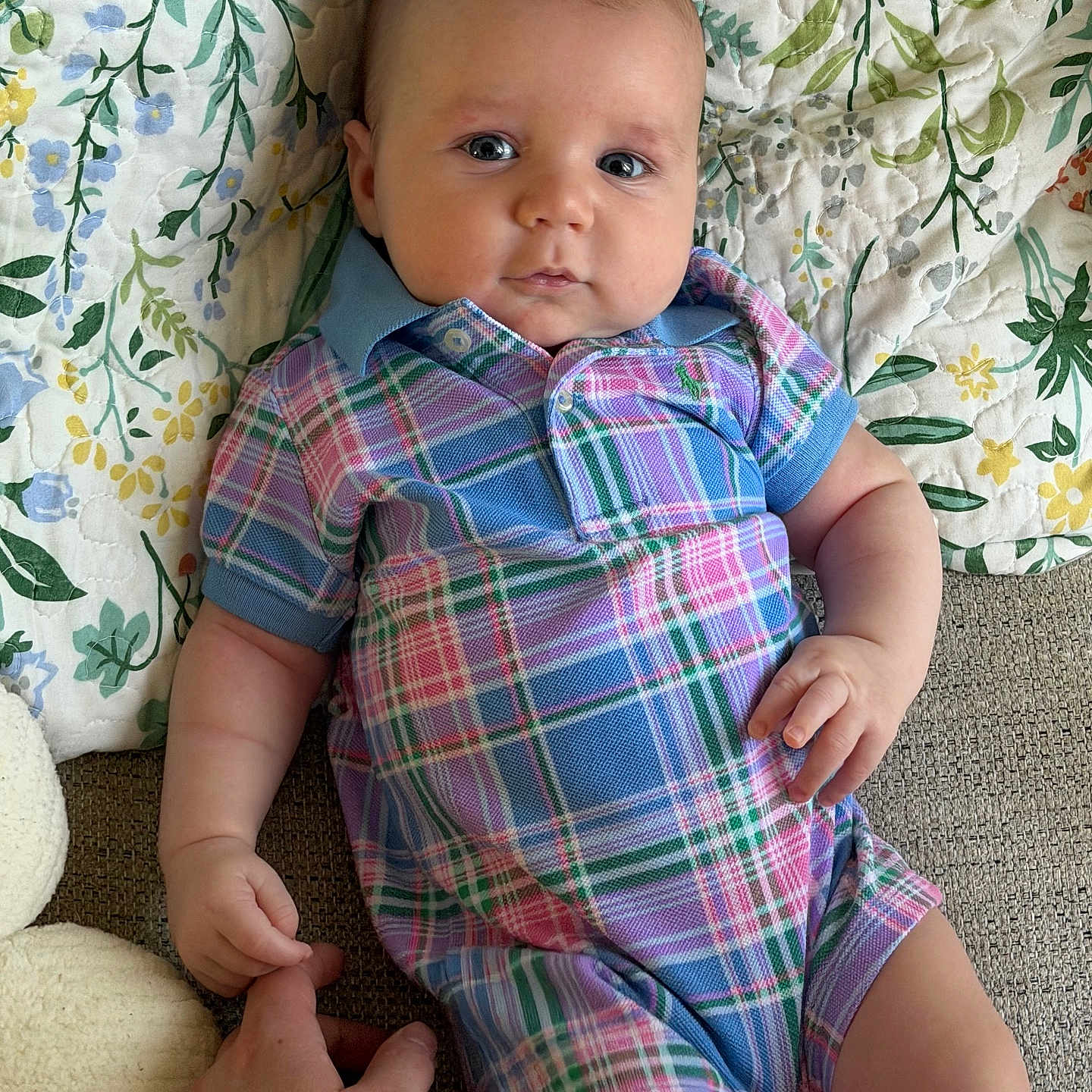 Noah joined the competition — help win amazing prizes! baby, infant, child, plaid, romper, hand, finger, quilt, floral_pattern, fabric, person, skin, face, eyes, cute, lying_down, holding, indoor, colorful, comfortable