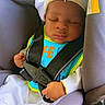 baby, car_seat, sleeping, child, bib, hat, safety_harness, infant, peaceful, cute, clothing, seatbelt, dove, religious_symbol, cross, indoors, portrait, young_child, resting, infant_clothing