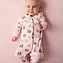 baby, bus_print, child, chubby_cheeks, cute, fabric_pattern, feet, footed_pajamas, hands, infant, lying_down, nursery, onesie, pink, portrait, product_photo, smiling, soft_lighting, striped_background, studio_photo