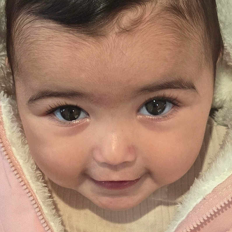 Lea participe au concours pour gagner de l'argent avec cette photo : apparel, baby, child, close_up, cute, eyes, face, fuzzy_lining, hair, indoors, infant, looking_up, pink_jacket, portrait, skin, smile, warm_clothing, warmth, young_child, zipper