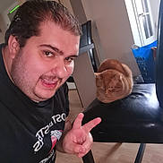 Bébé Ou Théo a rejoint le concours — aidez-le/la à gagner de superbes lots ! animal, black_tshirt, cat, chair, door, furniture, ginger_cat, hand_gesture, happy, home, indoor, laundry_basket, loaf_cat, man, peace_sign, person, pet, portrait, smiling, wood_floor
