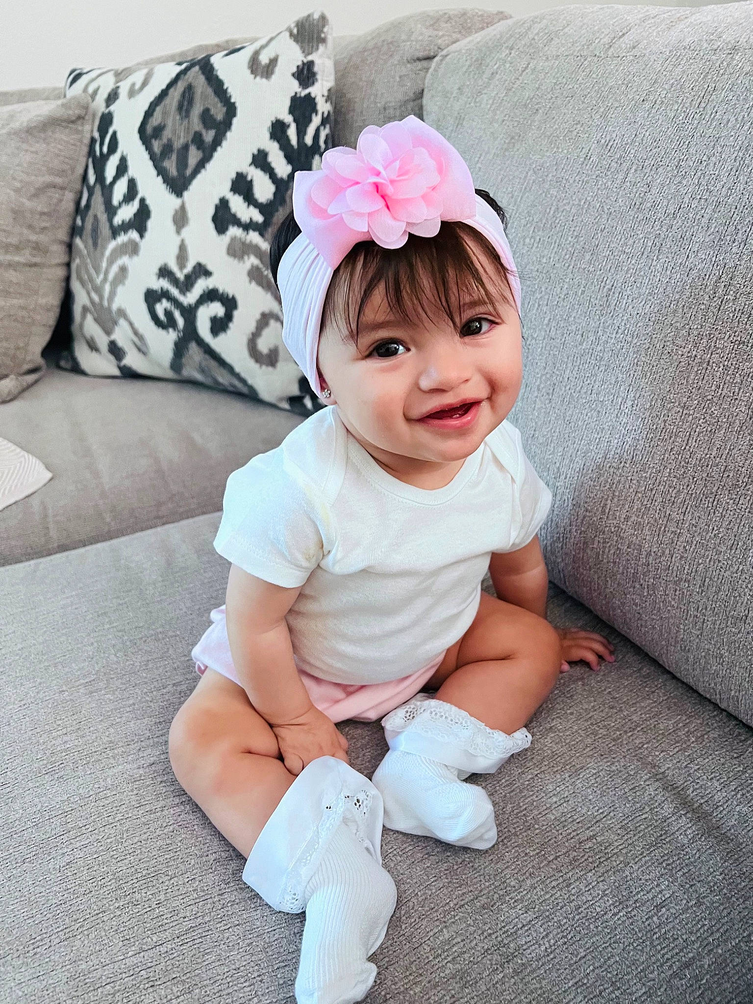 Aubrey is registered to the contest to win money with this photo: arm, baby, baby_toddler_clothing, couch, face, flower, hand, happy, headwear, human_leg, knee, pattern, person, petal, pink, skin, sleeve, smile, sock, textile