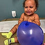 Ahaziah joined the competition — help win amazing prizes! toddler, child, balloon, smile, yellow_socks, curly_hair, indoor, cushioned_surface, playful, happy, person, portrait, blue_balloon, baby, hand, toy, cute, sitting, expression, skin