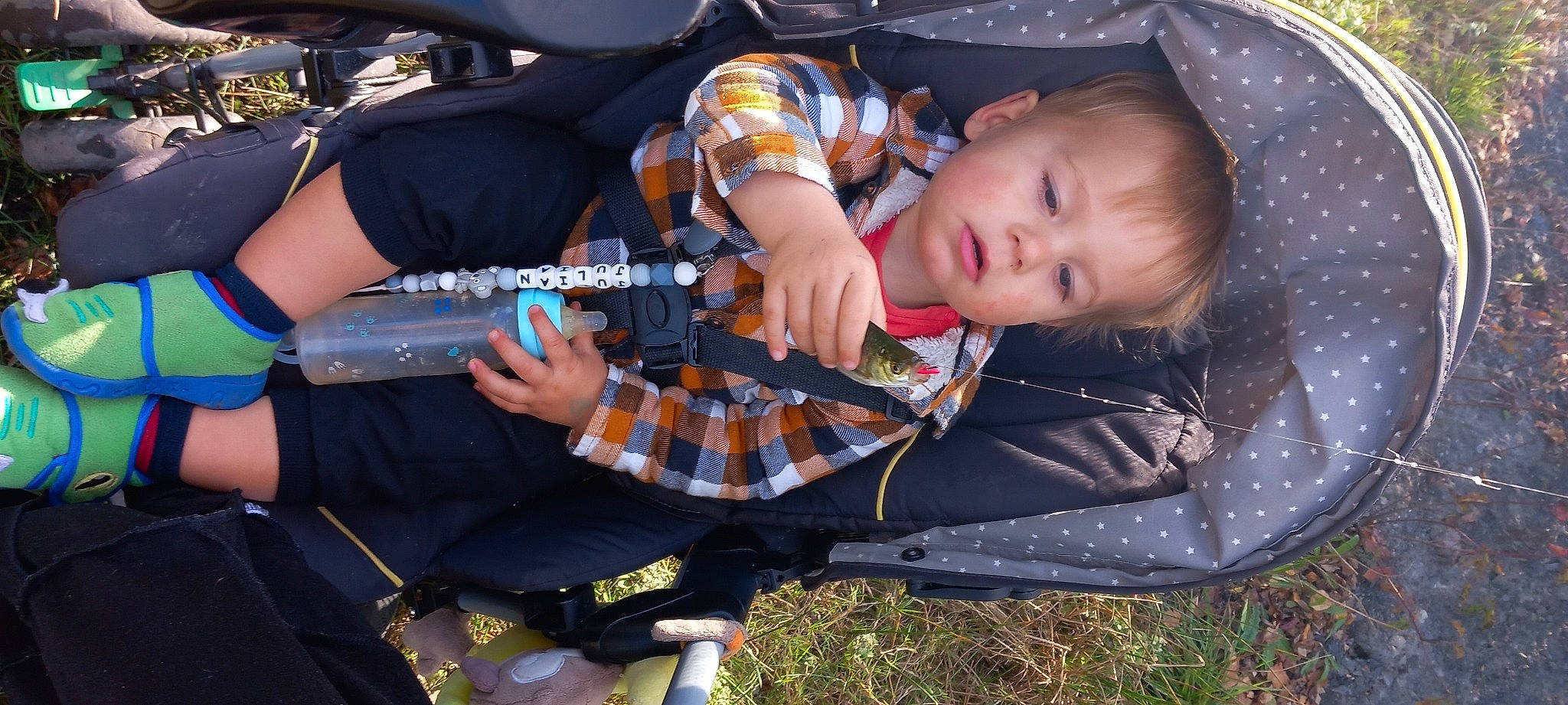 Julian a rejoint le concours — aidez-le/la à gagner de superbes lots ! baby, baby_carriage, baby_products, baby_toddler_clothing, child, comfort, cool, fun, grass, lap, musical_instrument, pattern, person, plaid, plant, plucked_string_instruments, recreation, sitting, tartan, toddler