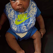 Andre Henry Jr is registered to the contest to win money with this photo: baby, infant, headband, nike, bib, blue_clothing, sitting, barefoot, dark_background, cute, child, portrait, person, indoors, expression, skin, foot, hand, face, young