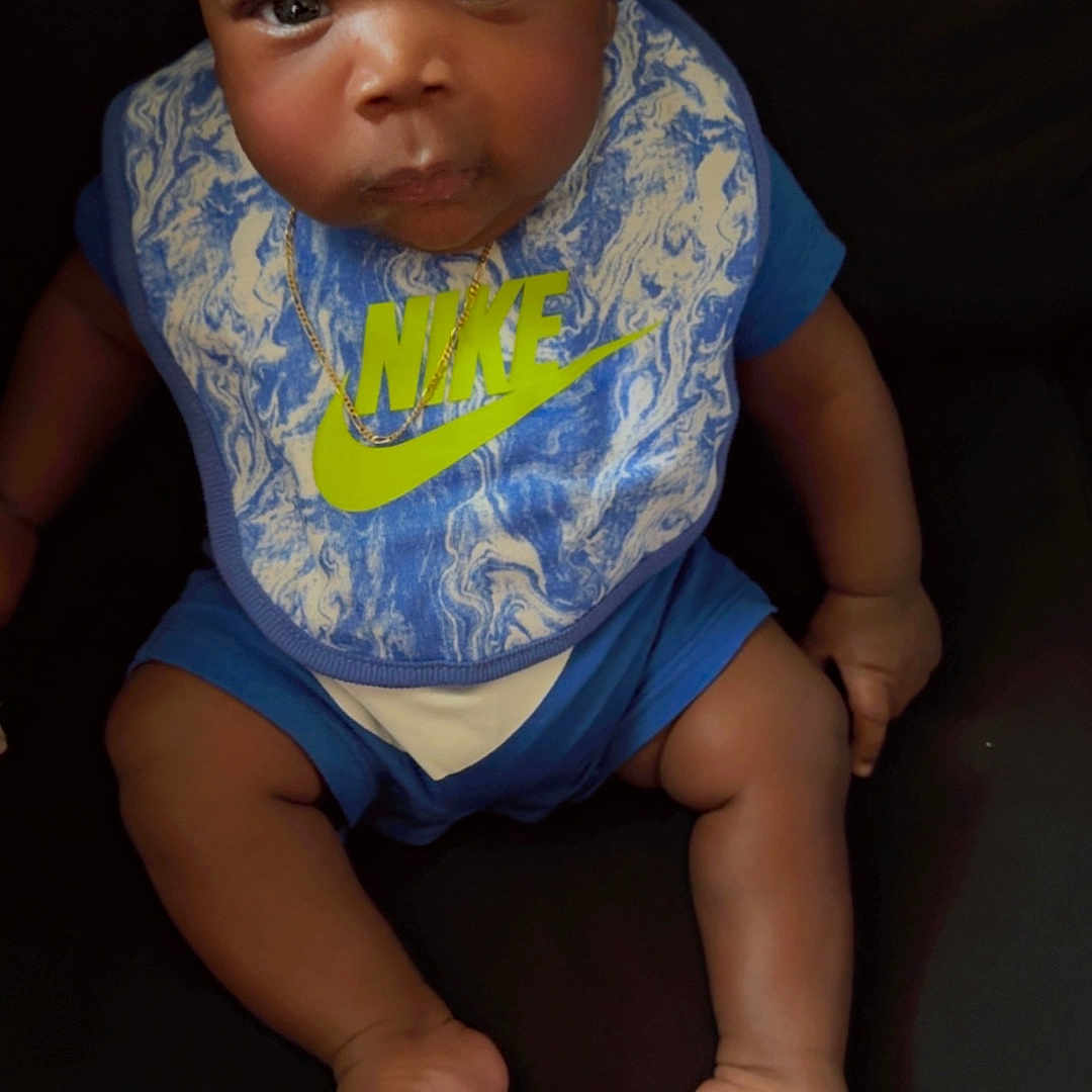 Andre Henry Jr is registered to the contest to win money with this photo: baby, barefoot, bib, blue_clothing, child, cute, dark_background, expression, face, foot, hand, headband, indoors, infant, nike, person, portrait, sitting, skin, young
