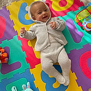 Zayn participe au concours pour gagner de l'argent avec cette photo : baby, infant, child, playmat, numbers, colorful, toy, plush_bunny, smile, face, hooded_sweater, knitted_clothes, carpet, sunlight, shadow, lying_down, playtime, happy, indoor, cute